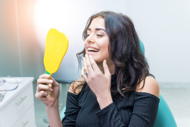 Woman looking at her dental implants in a mirror