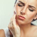 Woman holding her cheek, trying to comfort the pain of a tooth abscess.