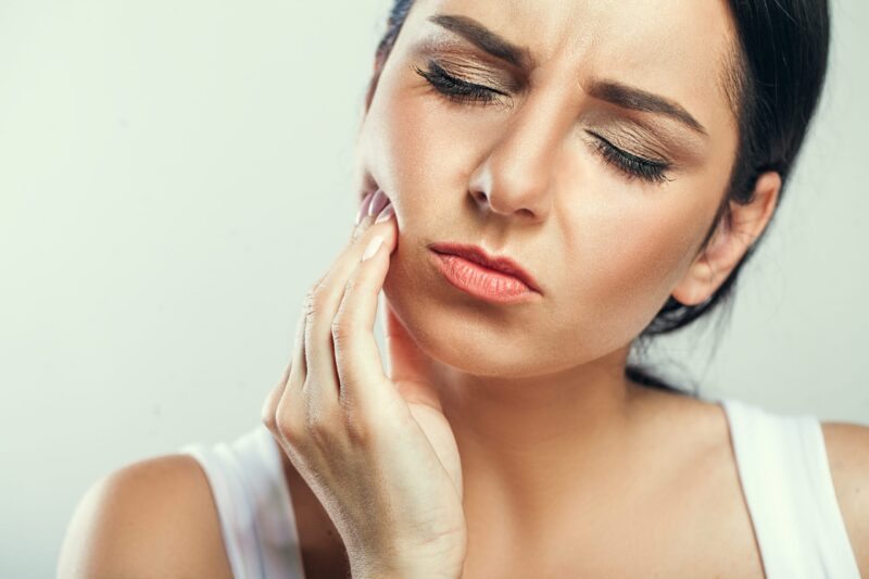 Woman holding her cheek, trying to comfort the pain of a tooth abscess.