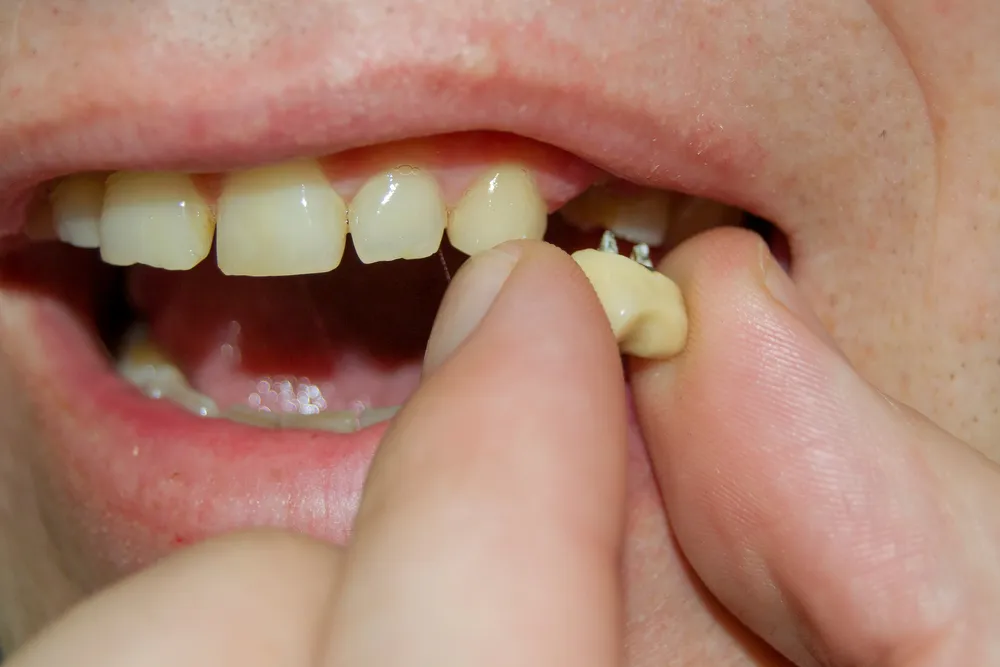 A person holding a tooth in one hand and a toothbrush in the other, demonstrating dental hygiene practices.