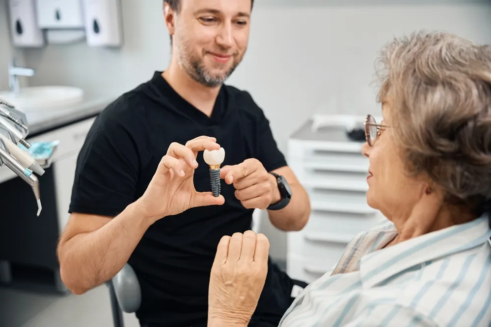 A man gently holds a toothbrush, offering it to an older woman, suggesting assistance with her dental care.