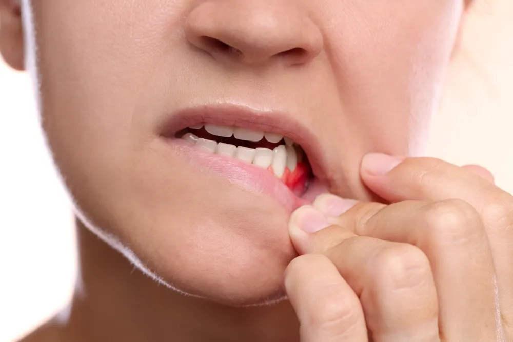 A woman holds a red toothbrush to her mouth, preparing to brush her teeth.