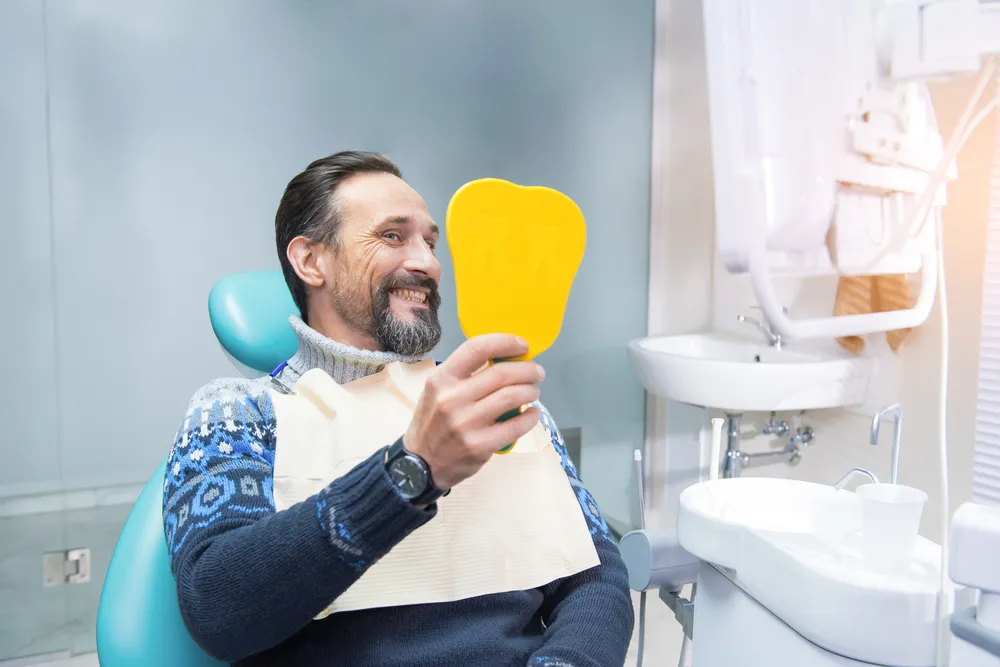 A man seated in a dental chair holds a yellow toothbrush, preparing for a dental check-up.