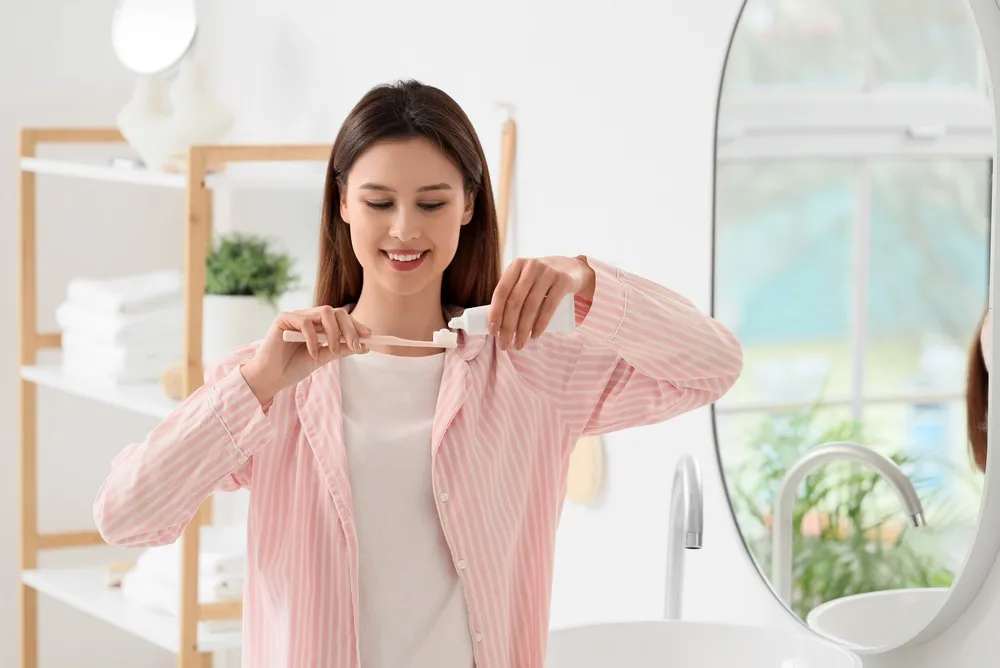 A woman in a pink robe is brushing her teeth in a bathroom mirror, focusing on her dental hygiene routine.